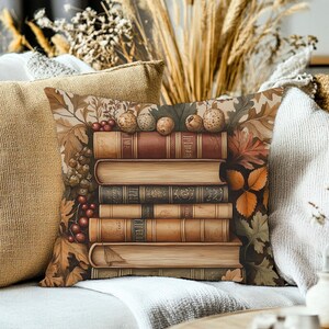 May include: A square throw pillow featuring a stack of five vintage-style books centered on a background of autumn leaves, berries, and acorns. The books have brown, tan, and gold spines with visible page edges, surrounded by a warm-toned botanical pattern.
