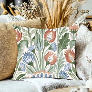 May include: A square throw pillow featuring a repeating botanical pattern on a cream background. The design displays stylized flowers in shades of muted coral and light blue, interspersed with long, flowing green leaves and stems.