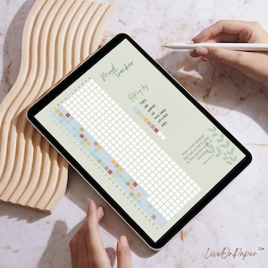 以下が含まれることがあります： スタイラス付きタブレットのデジタル気分トラッカー。トラッカーは、月の各日に対応する色付きの正方形で構成されたグリッドです。「Mood Tracker」と「Repong my day」のテキストが表示されています。「Even your darkest day has a role to play in the sacred work of becoming」のテキストも表示されています。