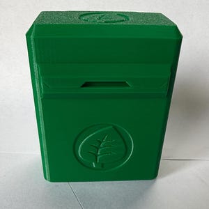 May include: A bright green, rectangular box with a leaf logo. The box has a slot on the front and a leaf design on the top. The box is made of a solid, matte material.