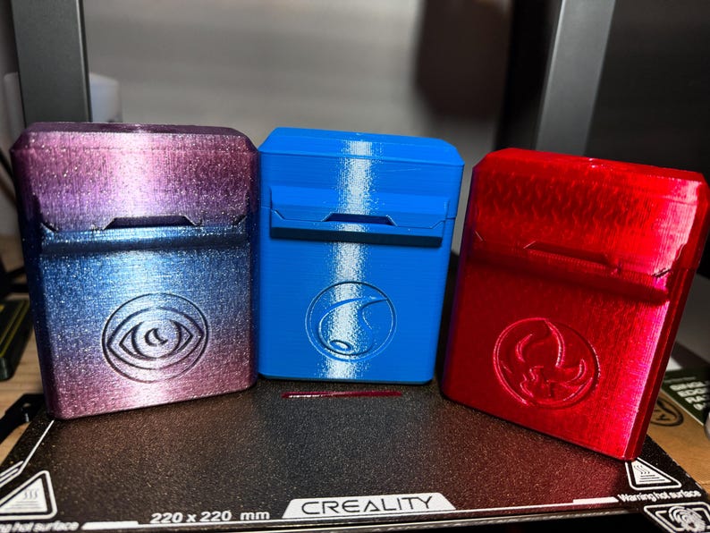 May include: Three 3D-printed rectangular cases in a row. The case on the left is a gradient of purple and blue with an eye symbol. The middle case is blue with a wave symbol. The case on the right is red with a symbol.
