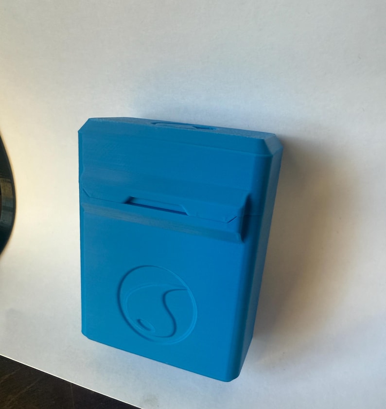 May include: A bright blue rectangular case with a curved design on the front. The case has a hinged lid with a small opening. The case is made of a solid material and appears to be 3D printed.
