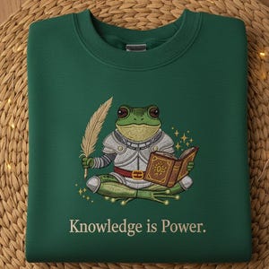 May include: A dark green sweatshirt with an embroidered design of a frog in armor holding a quill and a book. The text "Knowledge is Power" is below the frog.