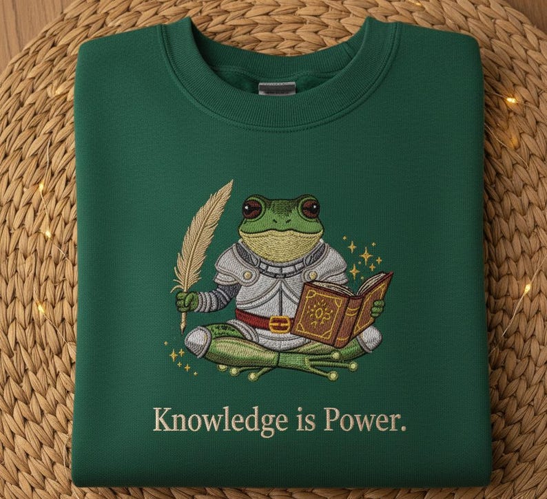May include: A dark green sweatshirt with an embroidered design of a frog in armor holding a quill and a book. The text "Knowledge is Power" is below the frog.