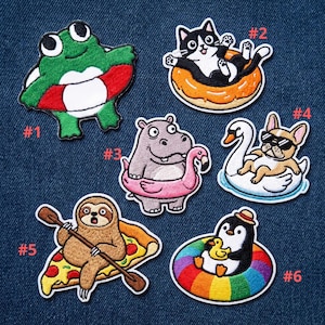 May include: Embroidered patches featuring various cartoon animals enjoying summer. Includes a frog with a life preserver, a cat on a donut float, a hippo with a flamingo float, a dog on a swan float, a sloth on a pizza, and a penguin with a rainbow float.