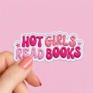 May include: Embroidered patch with the text "HOT GIRLS READ BOOKS" in shades of pink, outlined in white. The patch is held against a pink background. The text is in a playful, bubble-like font.