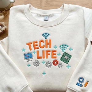 May include: Cream-colored sweatshirt with the words "TECH LIFE" in orange, along with computer-themed graphics. The design includes a computer monitor, gears, a circuit board, and WiFi symbols. A smaller design of a circuit board and USB drive is on the sleeve.
