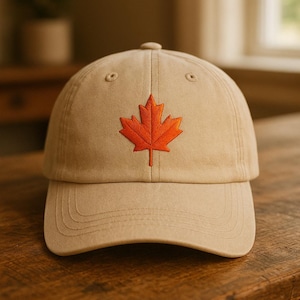 May include: A tan baseball cap with a curved brim and adjustable strap. The cap features an embroidered orange maple leaf on the front. The hat is made of a durable fabric and has a classic, casual style.