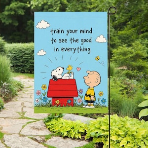 Może przedstawiać: Flaga ogrodowa z Snoopy'm i Woodstockiem na niebieskim tle z napisem "train your mind to see the good in everything". Flaga ma czerwony domek dla psa, kwiaty i Charlie'go Browna.