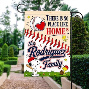 Könnte beinhalten: Eine Gartenflagge mit Baseball-Motiv mit dem Text "THERE IS NO PLACE LIKE HOME" und "the Rodriguez Family". Die Flagge zeigt einen Baseball, Snoopy mit einem Schläger und Woodstock. Das Design umfasst die Farben Rot, Weiß, Blau und Gelb.