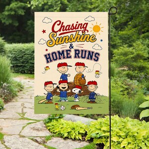Könnte beinhalten: Eine beige Gartenflagge mit Baseball-Motiv, die den Text "Chasing Sunshine & Home Runs" zeigt. Die Flagge zeigt Zeichentrickfiguren in Baseball-Kleidung, einen Baseball und einen Schläger. Die Flagge hängt in einem Garten.