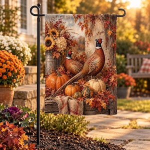 May include: A rectangular garden flag hanging on a black metal stand, featuring a printed autumn scene with two pheasants, orange pumpkins, sunflowers, and red maple leaves arranged on a rustic wooden surface with a fringed fabric accent.