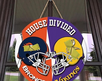 May include: Round wooden sign with a split design featuring football helmets. One side is orange with a navy helmet and the word "Broncos." The other side is purple with a gold helmet and the word "Vikings." The sign reads "House Divided."