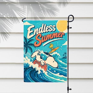 Może przedstawiać: Flaga ogrodowa przedstawiająca Snoopy'ego surfującego z Woodstockiem. Flaga ma niebieskie tło z napisem "Endless Summer" i żółtym słońcem. Palmy i fale dopełniają letnią scenerię.