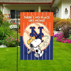 Pode incluir: Uma bandeira de jardim com Snoopy jogando beisebol. A bandeira tem um fundo laranja com o texto "THERE'S NO PLACE LIKE HOME!" e uma bola de beisebol com o logotipo do New York Mets. Listras azuis e brancas na parte inferior.