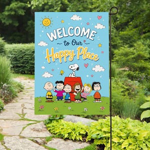 Może przedstawiać: Niebieska flaga ogrodowa z napisem "WELCOME to Our Happy Place" i postaciami z kreskówek, w tym Snoopy. Flaga ma tło nieba z chmurami, gwiazdami i sercami. Jest wyświetlana w ogrodzie.