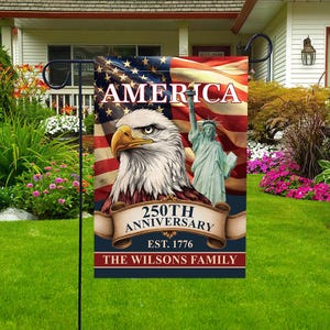 Può includere: Una bandiera da giardino patriottica con una bandiera americana, un'aquila calva e la Statua della Libertà. La bandiera recita "AMERICA" e "250TH ANNIVERSARY EST. 1776". Lo striscione in basso recita "THE WILSONS FAMILY".