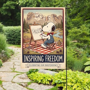 Może przedstawiać: Flaga ogrodowa z Snoopy'm, ubranym w kombinezon i czerwoną chustę, rysującym portret postaci historycznych przed Mount Rushmore. Na fladze widnieje napis "INSPIRING FREEDOM" i "CELEBRATING OUR INDEPENDENCE."