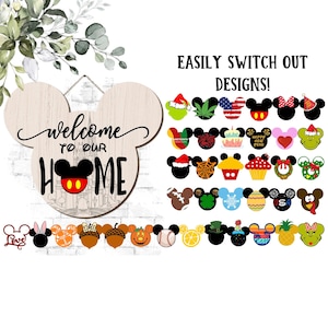Peut inclure: Un panneau en bois en forme de tête de souris avec le texte welcome TO OUR HOME et une icône de souris centrale. En dessous et à droite se trouvent de nombreux inserts interchangeables en forme de souris avec divers motifs saisonniers.