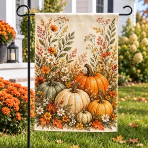 May include: A rectangular garden flag featuring a cream-colored background with a printed illustration of four pumpkins in shades of orange, green, and white, surrounded by autumn wildflowers, dried grasses, and fallen leaves in warm seasonal tones.