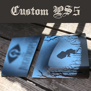 Op de afbeelding: Een aangepaste set zwarte en blauwe spelconsole-frontplaten met het silhouet van een figuur die door een bos met kale bomen loopt. De tekst Custom PS5 staat bovenaan in een gotisch lettertype en een wazig logo is zichtbaar op het linkerpaneel.
