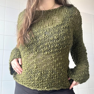 May include: Olive green knitted sweater with a textured, open weave design. The long-sleeved top has a boat neck and a slightly loose fit. The sweater is made of a soft, possibly natural fibre, and is suitable for casual wear.