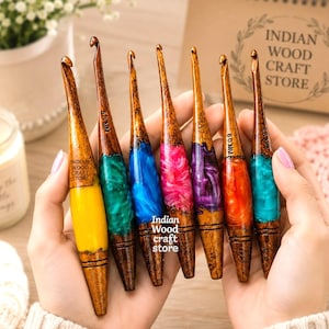May include: Seven handcrafted crochet hooks featuring polished wooden handles with colourful, swirling resin inserts in yellow, green, blue, pink, purple, orange, and teal. Each hook is engraved with the text Indian Wood Craft Store and size.
