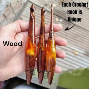 Op de afbeelding: Drie handgemaakte haaknaalden met een combinatie van donkerbruin hout en doorschijnende oranje hars. De naalden hebben een gladde, gepolijste afwerking en één naald is gemarkeerd met 4.0mm. De tekst op de afbeelding luidt Wood, Each Crochet Hook is Unique en Indian Wood craft store.