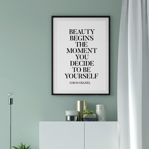 May include: A black framed print with a white background and black text that reads "Beauty begins the moment you decide to be yourself. Coco Chanel."