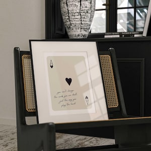 Op de afbeelding: Een ingelijste print van een aas schoppen speelkaart met de tekst "you can't change the cards you are dealt. just the way you play the hand".