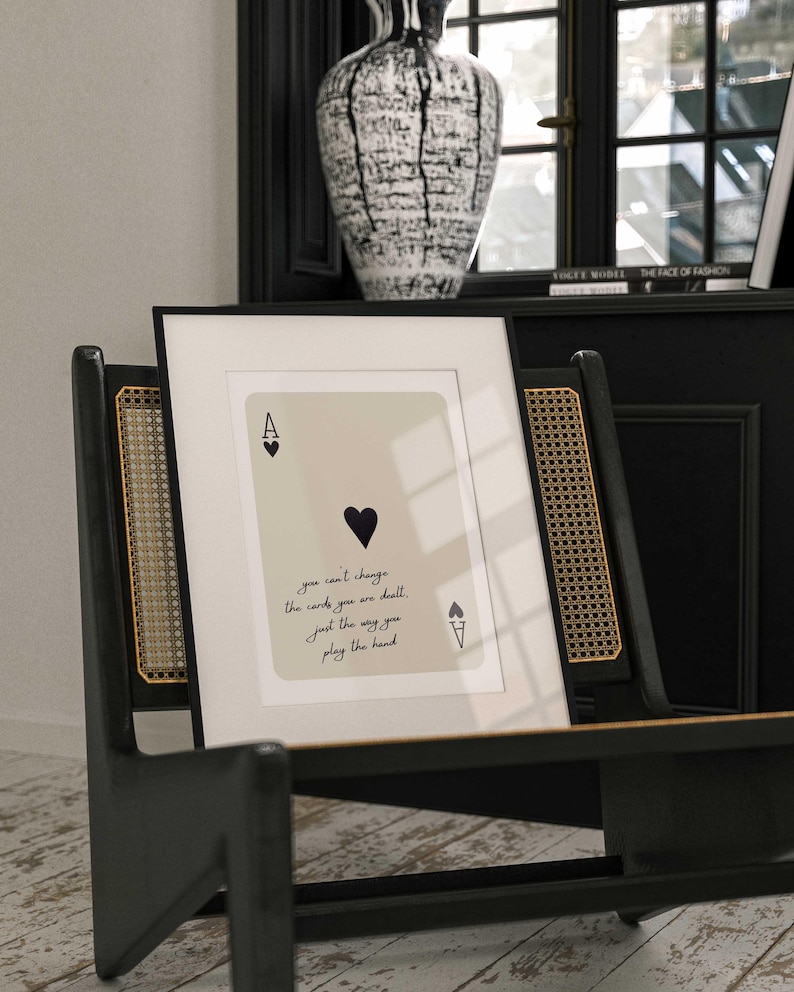Op de afbeelding: Een ingelijste print van een aas schoppen speelkaart met de tekst "you can't change the cards you are dealt. just the way you play the hand".