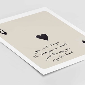 Op de afbeelding: Een beige achtergrond met een zwarte aas van harten speelkaart. De kaart heeft de tekst "you can't change the cards you are dealt, just the way you play the hand".