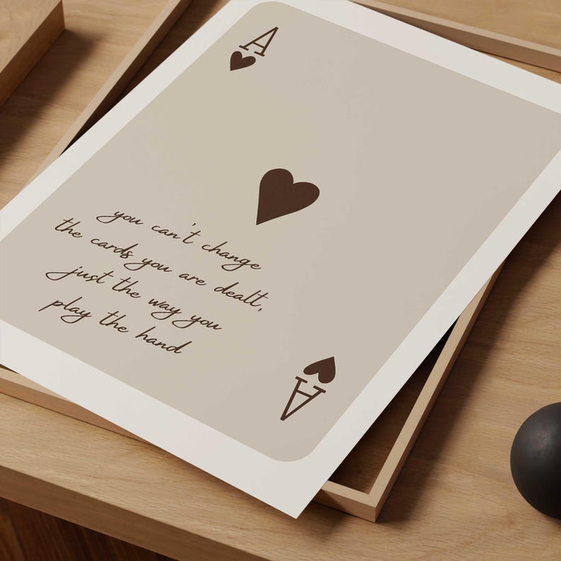 Op de afbeelding: Een beige printbare kunstprint met een bruin aas van harten speelkaartenontwerp. De print bevat de quote "Je kunt de kaarten die je krijgt niet veranderen, alleen de manier waarop je de hand speelt."