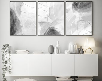 May include: Three black and white abstract art prints with a gray background and black lines. The prints are framed in black and are hanging on a white wall above a white cabinet.