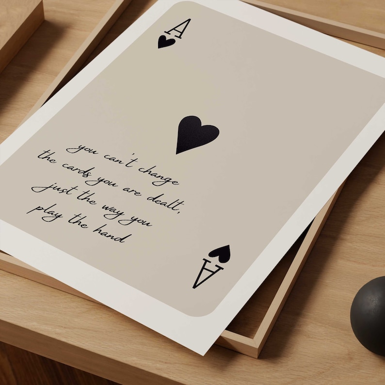 Op de afbeelding: Een beige kaart met een zwarte schoppen aas en de quote "Je kunt de kaarten die je krijgt niet veranderen, alleen de manier waarop je de hand speelt".