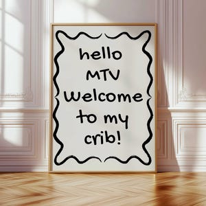 May include: A white framed poster with black text that reads "hello MTV welcome to my crib!" The text is written in a handwritten style and is surrounded by a black wavy border.