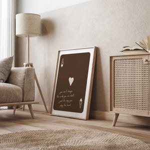 May include: A framed print of the Ace of Hearts playing card, in shades of brown and white. The card features the Ace symbol, a heart, and the text: "you can't change the words you are dealt, just the way you play the hand."