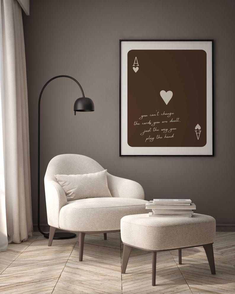 May include: A framed Ace of Hearts playing card art print with the text "you can't change the cards you are dealt, just the way you play the hand." The print hangs above a beige armchair and ottoman.