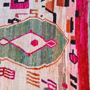 May include: A colorful Moroccan rug with geometric patterns in shades of pink, green, orange, and white. The rug has a distressed, vintage look and is made of wool.