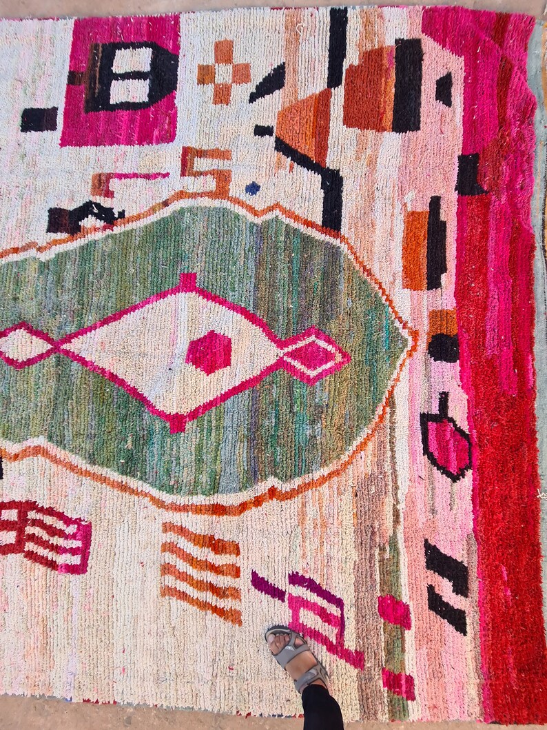 May include: A colorful Moroccan rug with geometric patterns in shades of pink, green, orange, and white. The rug has a distressed, vintage look and is made of wool.