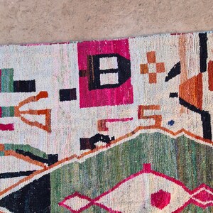 May include: A colorful rug with geometric patterns in shades of red, orange, green, black, and white. The rug has a cream-colored background.