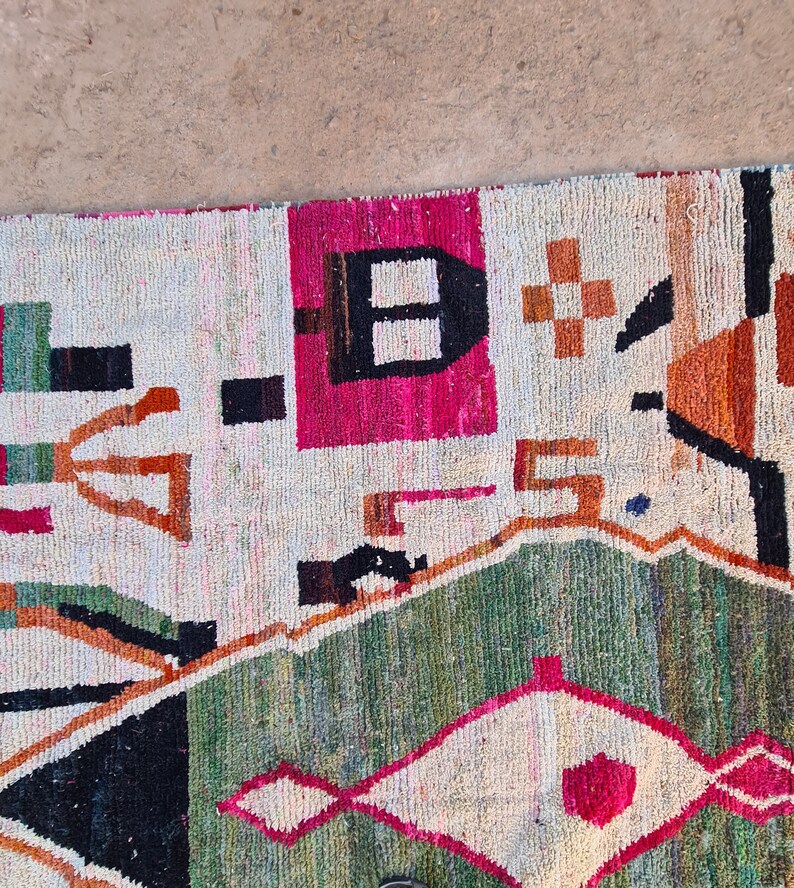 May include: A colorful rug with geometric patterns in shades of red, orange, green, black, and white. The rug has a cream-colored background.
