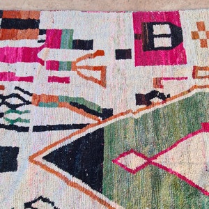 May include: A white rug with a geometric pattern in shades of pink, orange, green, and black. The rug has a distressed look and is made of wool.