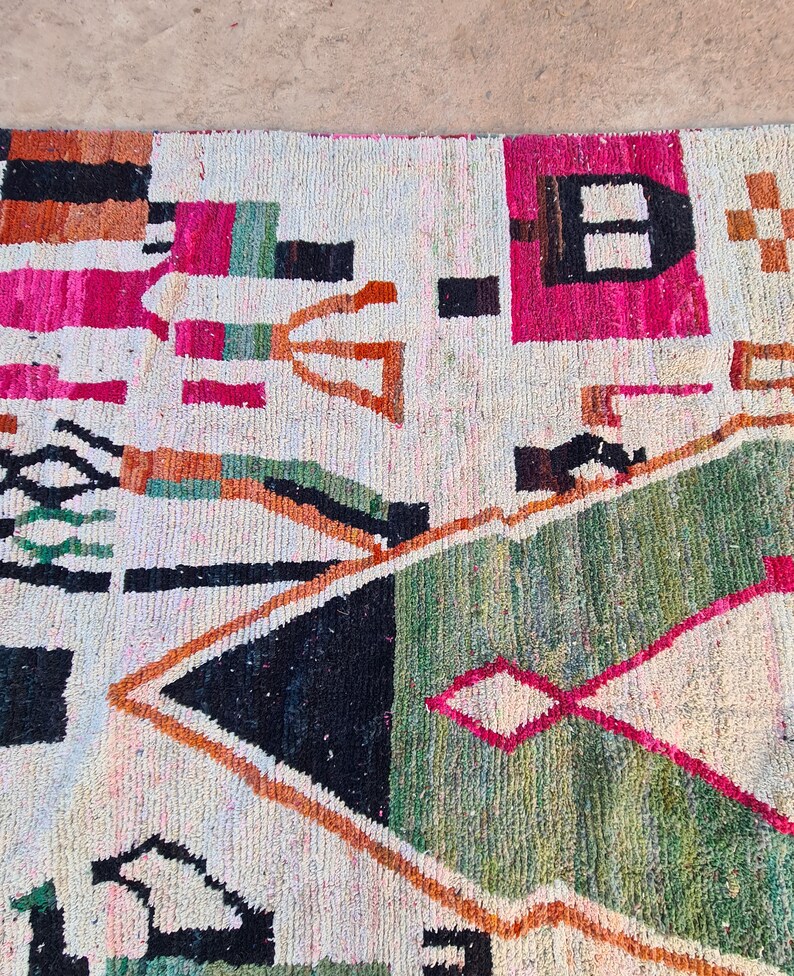 May include: A white rug with a geometric pattern in shades of pink, orange, green, and black. The rug has a distressed look and is made of wool.