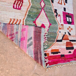 May include: A colorful rug with geometric patterns in shades of pink, green, orange, and black. The rug has a fringe border and is folded in half.