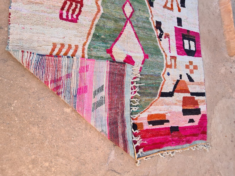 May include: A colorful rug with geometric patterns in shades of pink, green, orange, and black. The rug has a fringe border and is folded in half.