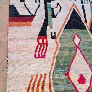 May include: A colorful rug with geometric patterns in shades of red, orange, green, black, and white. The rug has a cream background and is woven with a variety of textures.