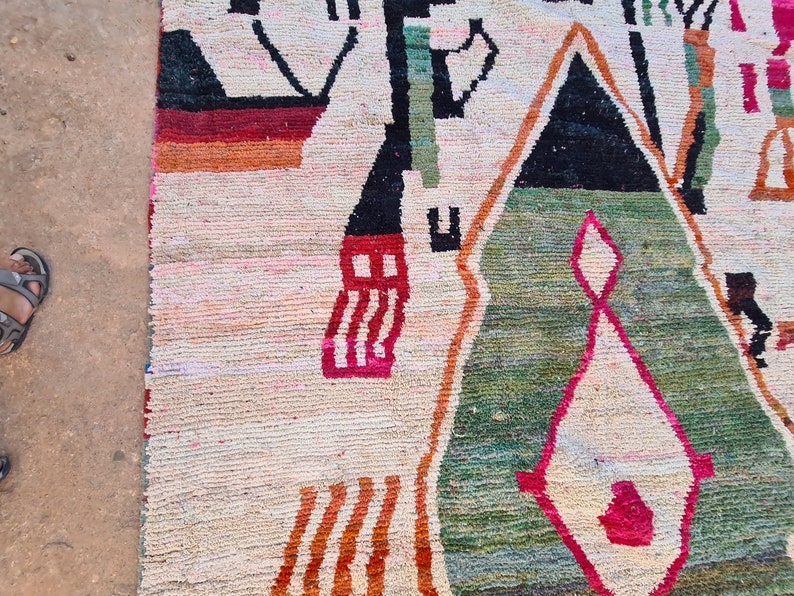 May include: A colorful rug with geometric patterns in shades of red, orange, green, black, and white. The rug has a cream background and is woven with a variety of textures.