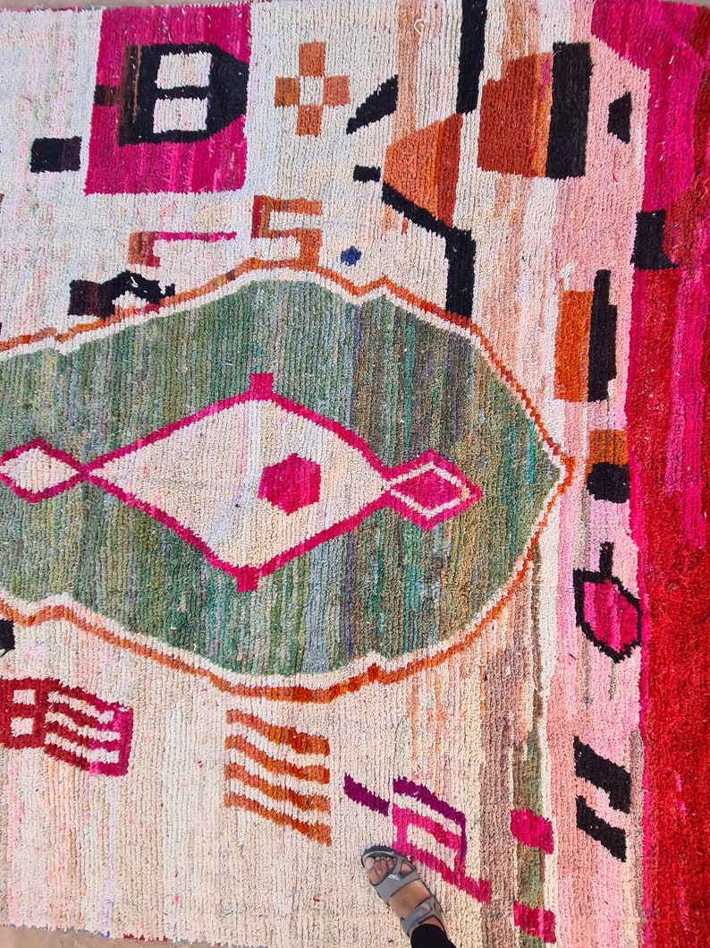 May include: A colorful rug with a geometric pattern in shades of pink, green, orange, and white. The rug has a diamond-shaped design in the center.