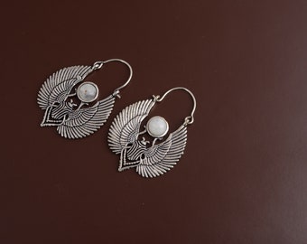 May include: A pair of silver hoop earrings with a white stone in the center of each earring. The earrings are shaped like wings.